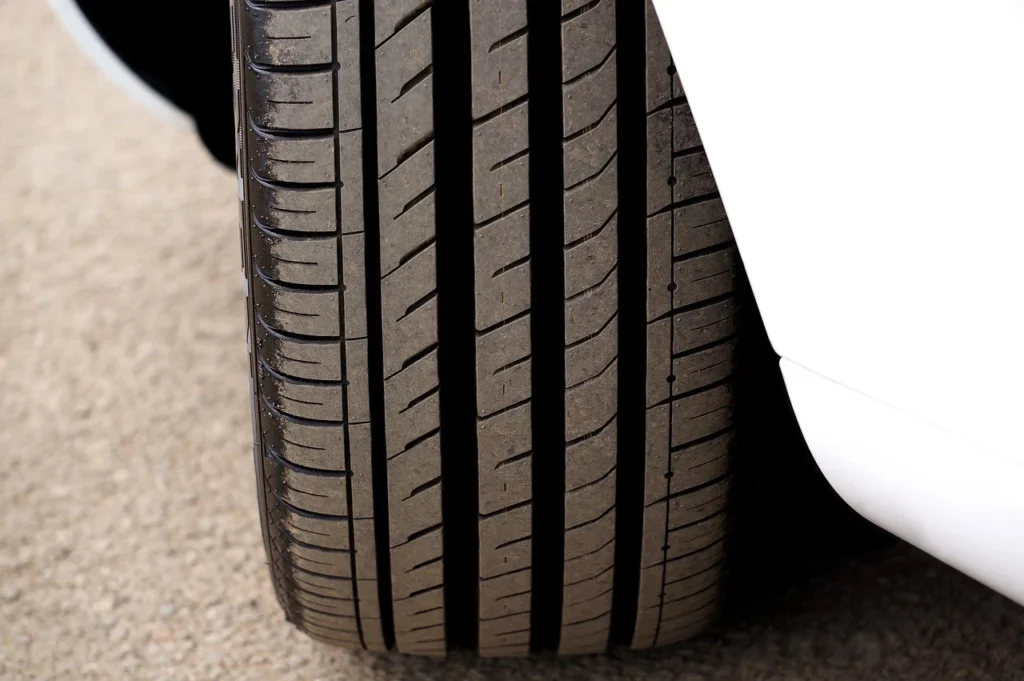 Close up of a driver checking car tyre tread depth using a coin against the tread grooves