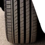 Close up of a driver checking car tyre tread depth using a coin against the tread grooves