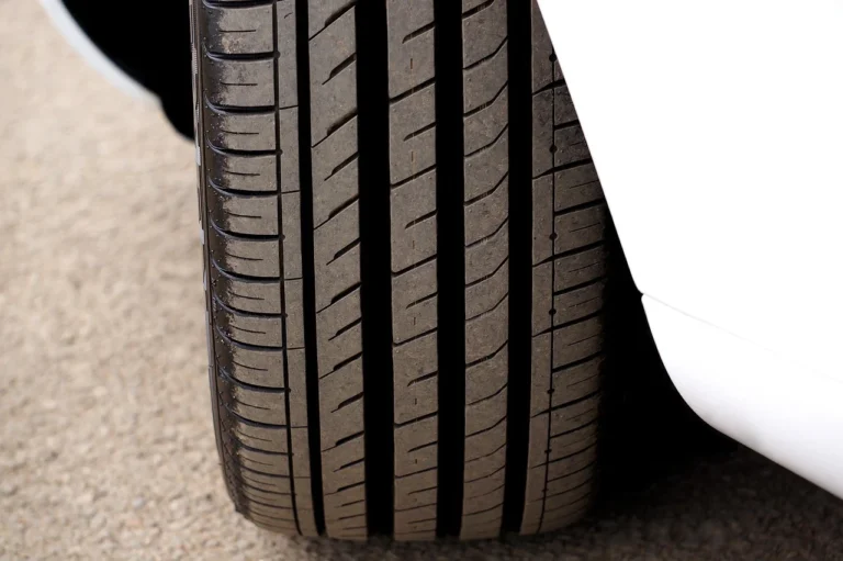 Close up of a driver checking car tyre tread depth using a coin against the tread grooves