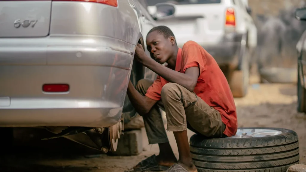 A young mechanic works on a car's underside in an outdoor garage setting — SSK Mechanics guide to BMW 3 Series Brake Pads, Discs and Calipers Guide