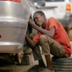 A young mechanic works on a car's underside in an outdoor garage setting — SSK Mechanics guide to BMW 3 Series Brake Pads, Discs and Calipers Guide