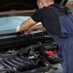 A mechanic in blue overalls works on a car engine outdoors, showcasing vehicle maintenance skills — SSK Mechanics guide to Honda Jazz Battery Check and Car-Not-Starting Guide