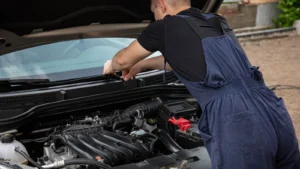 A mechanic in blue overalls works on a car engine outdoors, showcasing vehicle maintenance skills — SSK Mechanics guide to Honda Jazz Battery Check and Car-Not-Starting Guide