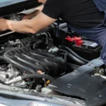 Mechanic in blue overalls working on car engine with open hood outdoors during the day — SSK Mechanics guide to Hyundai i10 Battery Check and Car-Not-Starting Guide