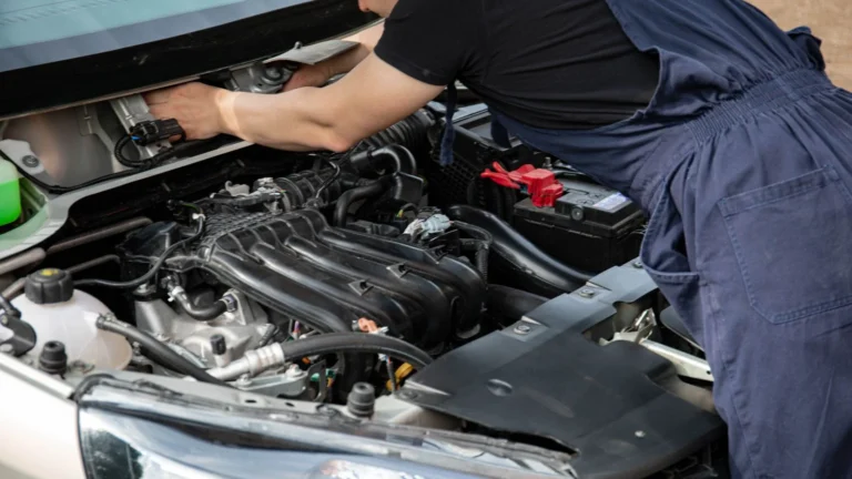 Mechanic in blue overalls working on car engine with open hood outdoors during the day — SSK Mechanics guide to Hyundai i10 Battery Check and Car-Not-Starting Guide