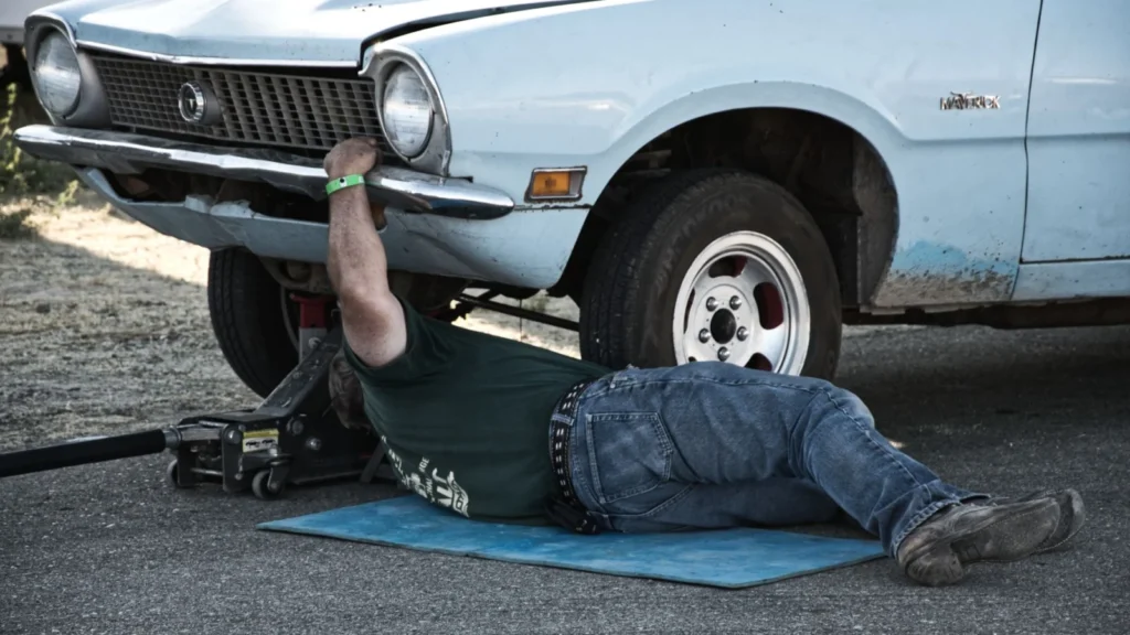 A mechanic working under a classic car on the pavement during the day — SSK Mechanics guide to Peugeot 208 Brake Pads, Discs and Calipers Guide