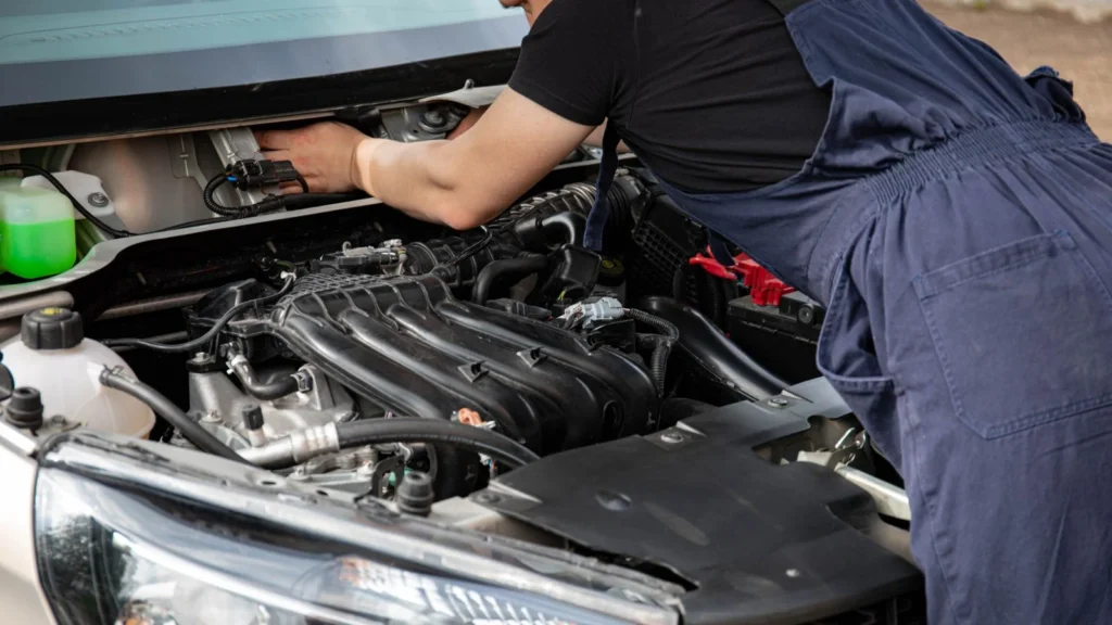 Mechanic in blue overalls repairing a car engine under the hood outdoors — SSK Mechanics guide to Hyundai Tucson Battery Check and Car-Not-Starting Guide
