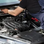Mechanic in blue overalls repairing a car engine under the hood outdoors — SSK Mechanics guide to Hyundai Tucson Battery Check and Car-Not-Starting Guide