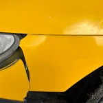 Close-up of dented yellow car bodywork after impact damage