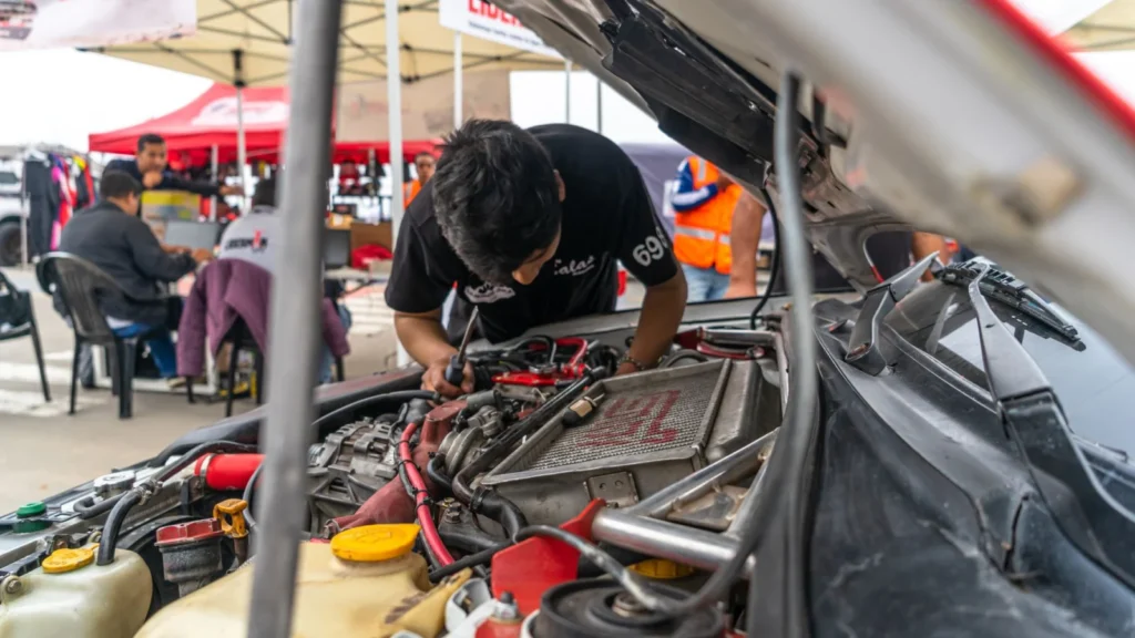 Mechanic inspecting a car engine outdoors at an automotive workshop. Team members in the background — SSK Mechanics guide to Car Symptom & Fault Guide: What Every Noise, Smell and…