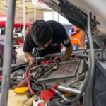 Mechanic inspecting a car engine outdoors at an automotive workshop. Team members in the background — SSK Mechanics guide to Car Symptom & Fault Guide: What Every Noise, Smell and…