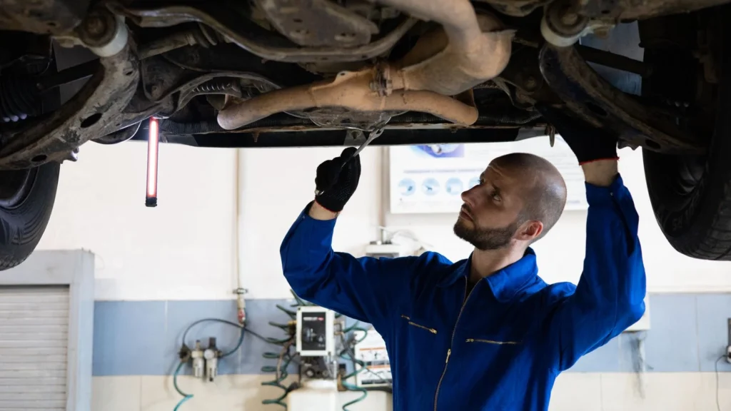A mechanic in blue overalls inspects the exhaust system of a car in a workshop — SSK Mechanics guide to What Does White Smoke From the Exhaust Mean