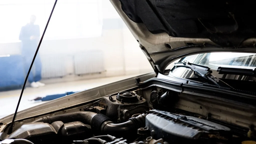 Detailed image of a car engine underneath the open hood in a well-lit indoor garage — SSK Mechanics guide to What Does Blue Smoke From the Exhaust Mean