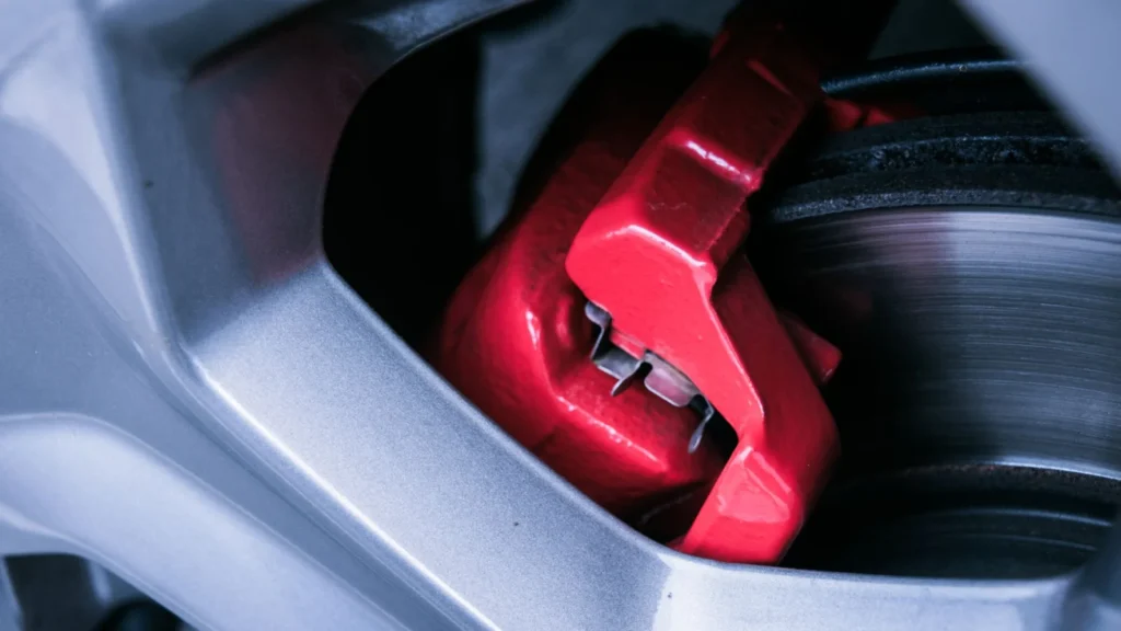 Detailed photo of a red automotive brake caliper and disc brake in focus — SSK Mechanics guide to Why Do My Brakes Smell Like They're Burning