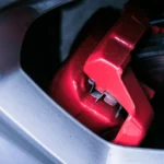 Detailed photo of a red automotive brake caliper and disc brake in focus — SSK Mechanics guide to Why Do My Brakes Smell Like They're Burning