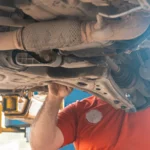 Mechanic working under a vehicle, inspecting the undercarriage in a repair garage, ensuring… — SSK Mechanics guide to Why Is My Brake Pedal Sinking to the Floor