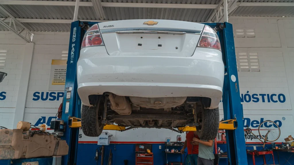 A white Chevrolet car is lifted for maintenance in an automotive repair shop — SSK Mechanics guide to How Mobile MOT Collection and Return Works