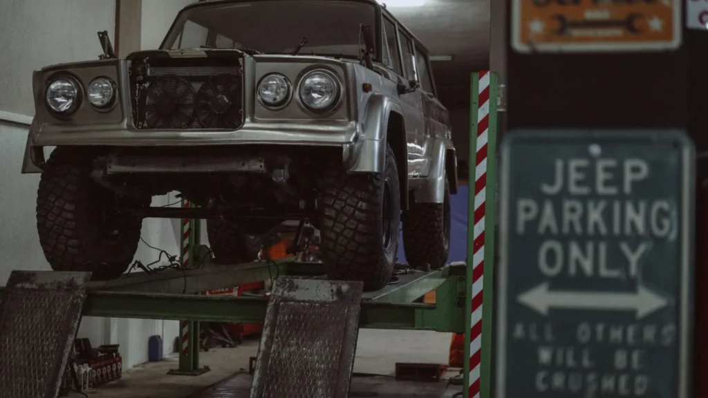 Classic Jeep on a lift in an indoor auto repair shop with a humorous parking sign — SSK Mechanics guide to Car Maintenance Calendar: What to Check Every Month, Season…