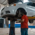 Two mechanics inspecting a white car on a lift inside a garage workshop — SSK Mechanics guide to How Often Should You Service Your Car? A UK Guide