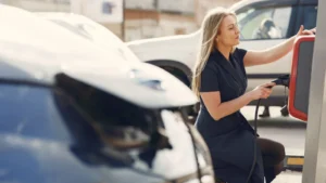 Side view of full length female driver in casual dress squatting near station while charging… — SSK Mechanics guide to Electric & Hybrid Car Maintenance: What Actually Needs Servicing