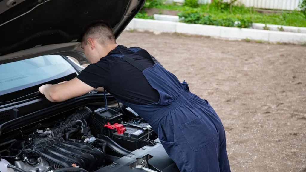 Mechanic in blue coveralls working on a car engine outdoors, focused on repair — SSK Mechanics guide to What Happens During a Hybrid Battery Health Check