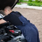 Mechanic in blue coveralls working on a car engine outdoors, focused on repair — SSK Mechanics guide to What Happens During a Hybrid Battery Health Check