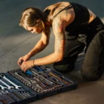 Young tattooed woman in black tank top organizing tools from a toolbox beside a motorcycle — SSK Mechanics guide to What to Expect When a Mobile Mechanic Comes to You