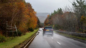 Car driving down a wet road surrounded by colorful autumn trees under a cloudy sky — SSK Mechanics guide to Driving in Bradford & West Yorkshire: What Local Roads Do to…