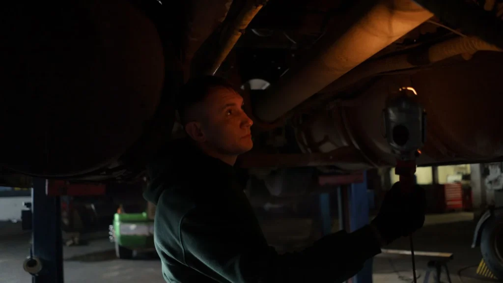 Mechanic working in dimly lit garage, inspecting car's undercarriage with a portable light source — SSK Mechanics guide to Spen Valley Roads: Pothole Damage Around Cleckheaton, Low…