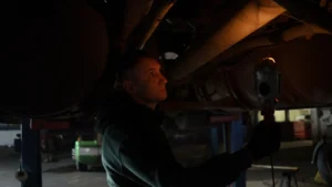 Mechanic working in dimly lit garage, inspecting car's undercarriage with a portable light source — SSK Mechanics guide to Spen Valley Roads: Pothole Damage Around Cleckheaton, Low…