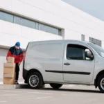 A delivery driver wearing a face mask unloads packages from a van outside a modern building — SSK Mechanics guide to The True Cost of a Van Off the Road: Downtime for Tradespeople