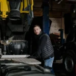 A mechanic in a puffer jacket works on a truck in a dimly lit workshop — SSK Mechanics guide to Braking System Care for Vans Carrying Heavy or Frequent Loads