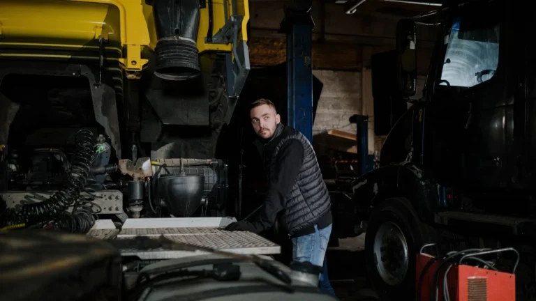 A mechanic in a puffer jacket works on a truck in a dimly lit workshop — SSK Mechanics guide to Braking System Care for Vans Carrying Heavy or Frequent Loads
