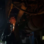 Mechanic examines vehicle underbody in dimly lit workshop, holding inspection light — SSK Mechanics guide to Why You Should Never Jack a Car Up Without Axle Stands