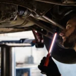 Mechanic using light to inspect vehicle undercarriage in workshop for maintenance — SSK Mechanics guide to Can You Bleed Your Own Brakes? What Competent DIYers Should Know