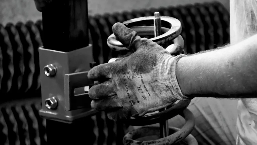 Close-up of a gloved auto mechanic's hand working with a spring in a workshop — SSK Mechanics guide to Knocking or Clunking Over Bumps: What's Going On Underneath