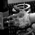 Close-up of a gloved auto mechanic's hand working with a spring in a workshop — SSK Mechanics guide to Knocking or Clunking Over Bumps: What's Going On Underneath