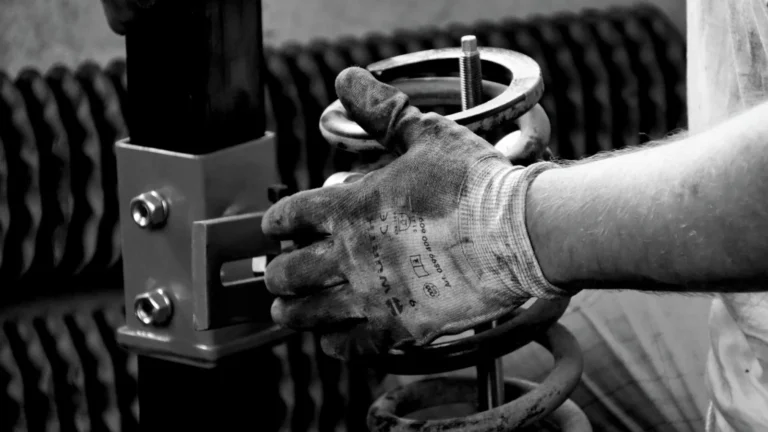 Close-up of a gloved auto mechanic's hand working with a spring in a workshop — SSK Mechanics guide to Knocking or Clunking Over Bumps: What's Going On Underneath