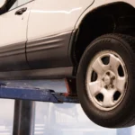 A white car suspended on a lift in an automotive repair shop, showcasing maintenance work — SSK Mechanics guide to Rattling Noise From Underneath the Car: What It Usually Means