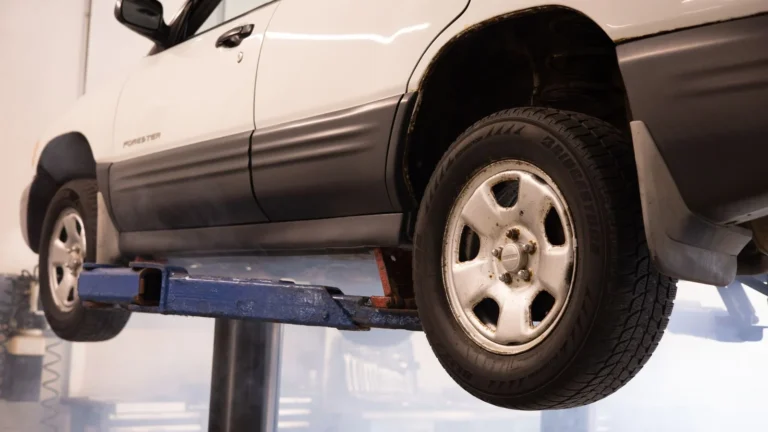 A white car suspended on a lift in an automotive repair shop, showcasing maintenance work — SSK Mechanics guide to Rattling Noise From Underneath the Car: What It Usually Means