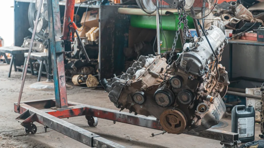 Close-up of a car engine hoisted in a mechanic's workshop, showcasing industrial tools — SSK Mechanics guide to Squealing Belt Noise on Startup: What It Means