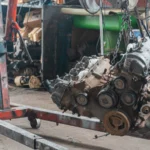 Close-up of a car engine hoisted in a mechanic's workshop, showcasing industrial tools — SSK Mechanics guide to Squealing Belt Noise on Startup: What It Means