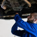 Mechanic in blue coveralls works under a car, focusing on repairs in a garage setting — SSK Mechanics guide to Humming Noise That Gets Louder With Speed? Likely a Wheel Bearing