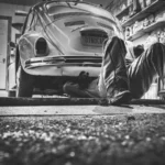 Mechanic working beneath a classic Volkswagen Beetle in a vintage garage setting — SSK Mechanics guide to SSK Mechanics vs ClickMechanic: How Mobile Mechanic Booking…