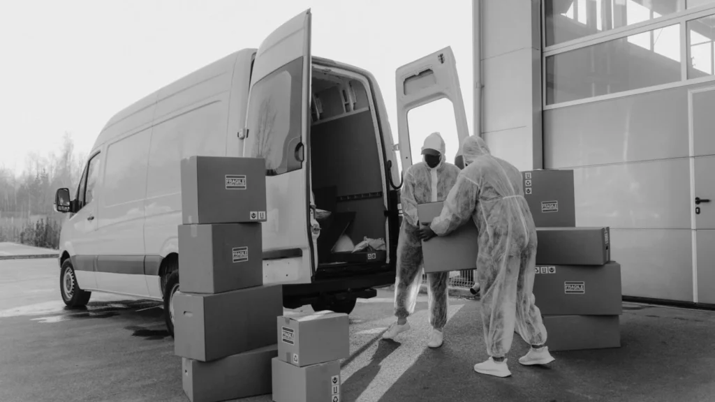 Two workers in PPE handling packages from a delivery van in a monochrome setting — SSK Mechanics guide to RAC Fleet Cover vs a Local Mobile Mechanic Partnership for…