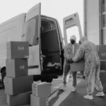 Two workers in PPE handling packages from a delivery van in a monochrome setting — SSK Mechanics guide to RAC Fleet Cover vs a Local Mobile Mechanic Partnership for…