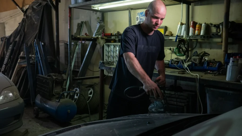 Bald mechanic focused on repairing a car engine in a garage setting — SSK Mechanics guide to Kwik Fit Leeds vs Mobile Servicing Across West Yorkshire