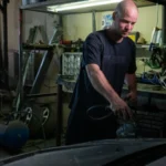 Bald mechanic focused on repairing a car engine in a garage setting — SSK Mechanics guide to Kwik Fit Leeds vs Mobile Servicing Across West Yorkshire
