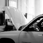 Black and white photo of a car in an auto repair shop. Hood open for maintenance — SSK Mechanics guide to Halfords vs Kwik Fit MOT: Which Is Better for Bradford Drivers
