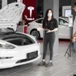 A customer talks with a sales representative about a Tesla Model 3 in a car dealership,… — SSK Mechanics guide to Main Dealer EV Servicing vs Independent Mobile EV…